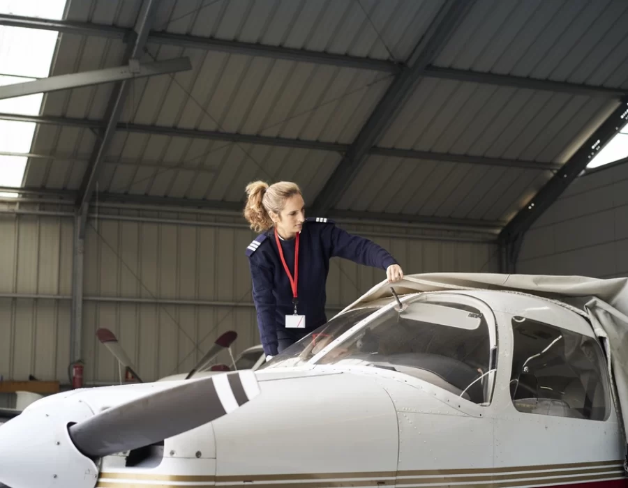 young-female-pilot-discovering-light-aircraft-with-protective-cover-hangar